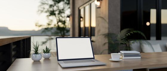 A laptop with a white screen mockup on a wooden table on a cozy contemporary home balcony.