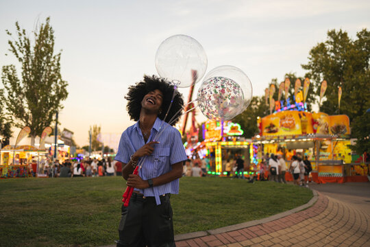Cheerful Afro man standing with balloons at amusement park