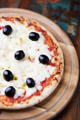 Pizza with mozzarella cheese and black olives on wooden background. Soft focus. Close up