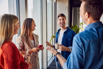Happy businessman holding coffee cup and talking to colleagues in office