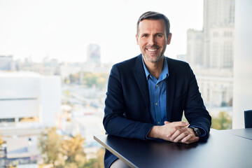 Smiling mature businessman sitting with hands clasped n office