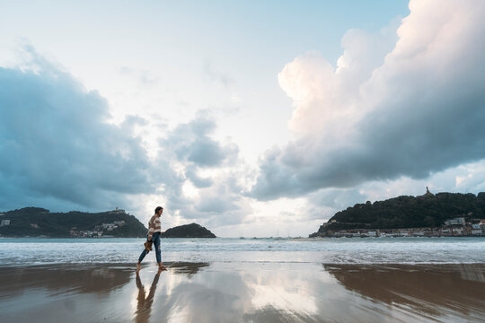Young woman walking on Playa de la Concha shore at sunset under cloudy sky