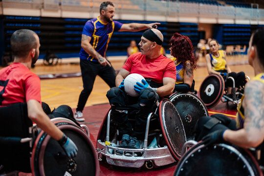 Coach giving instructions to men and women sitting on wheelchair at sports center