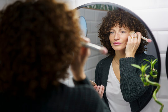 Woman with curly hair applying make-up in bathroom at home