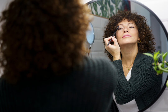 Woman applying eye make-up in bathroom at home