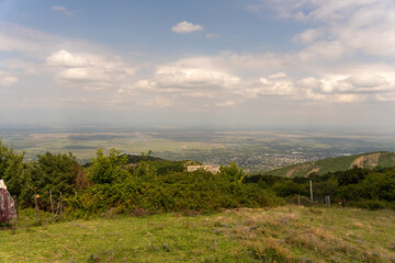 A view of a city from a hilltop. The sky is cloudy and the sun is shining