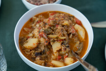 A bowl of food with a spoon in it. The bowl is white and the food is red and green