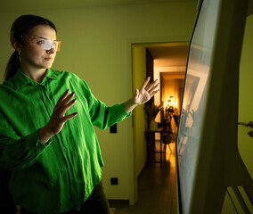 Woman with smart glasses and gesturing near device screen at home
