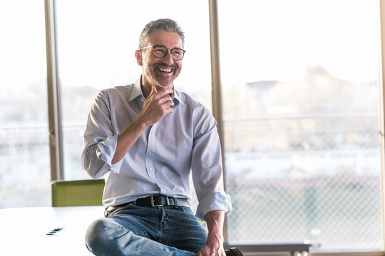Happy businessman sitting on table at office