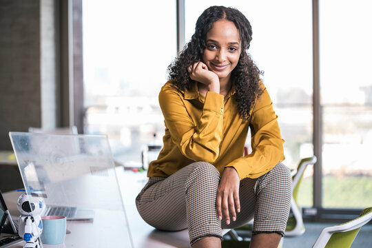 Young businesswoman with hand on chin sitting at desk in office