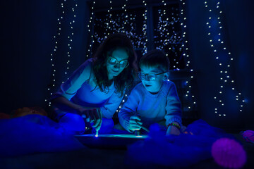Child and therapist in sensory stimulating room, black snoezelen. Autistic child playing with therapist during occupational therapy session.