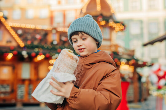 Boy in blue knit hat holding trdelnik at market during Christmas