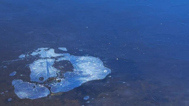 Stone flies onto thin ice, breaks it and leaves large splashes and cracks.