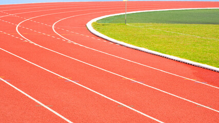 Red synthetic running tracks background with white curve lines pattern and green field in athletic...