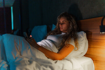 Obraz premium Young lady checking her phone before getting to sleep.