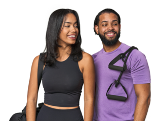 Young Latino couple ready for gym training looks aside smiling, cheerful and pleasant.