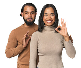 Young Latino couple in studio cheerful and confident showing ok gesture.