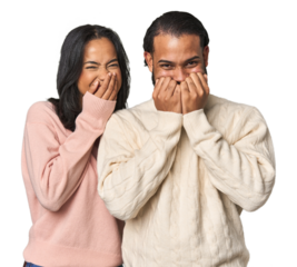 Young Latino couple in studio laughing about something, covering mouth with hands.