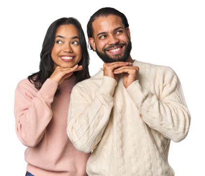 Young Latino couple in studio keeps hands under chin, is looking happily aside.