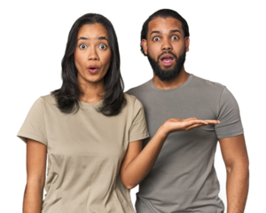 Young Latino couple in studio impressed holding copy space on palm.