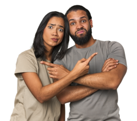 Young Latino couple in studio points sideways, is trying to choose between two options.