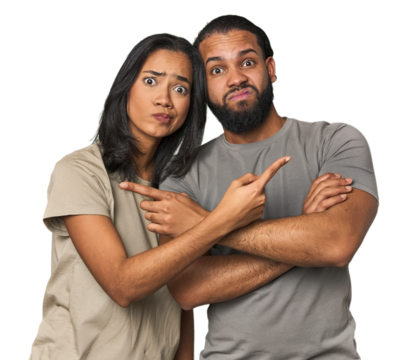 Young Latino couple in studio points sideways, is trying to choose between two options.