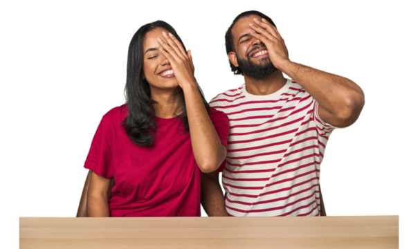 Seated young Latino couple at table laughing happy, carefree, natural emotion.