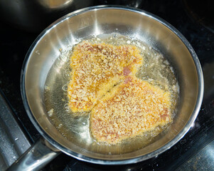 Frying schnitzel in hot oil in a steel pan, boiling oil with a piece of meat, cooking homemade...
