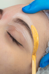 Hands of Professional Beautitian While Completing Eyebrow Correction with Wax and Wooden Sticks in Beauty Salon As Eyebrow Hair Removal with Wax.
