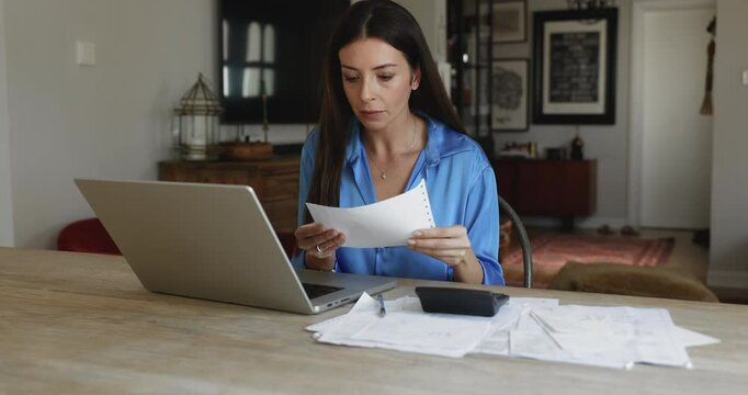 Focused woman sits at table with laptop, calculator, and papers spread out, reviewing and organizing documents, manage budget, pay bills using secure e-bank system. Responsibility, financial planning