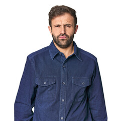 Studio portrait of young Hispanic male blows cheeks, has tired expression. Facial expression...