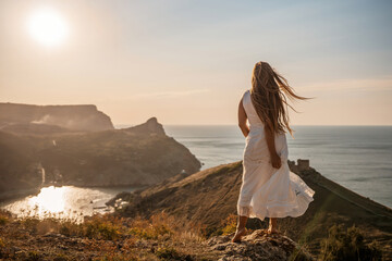 A woman in a white dress stands on a hill overlooking the ocean. The scene is serene and peaceful,...