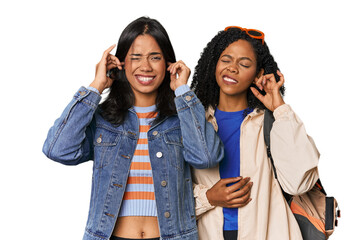 Latin friends ready for vacation covering ears with fingers, stressed and desperate by a loudly ambient.