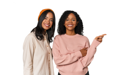 Young Latin friends together in studio smiling cheerfully pointing with forefinger away.