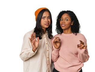 Young Latin friends together in studio rejecting someone showing a gesture of disgust.