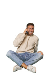 Caucasian man sitting on floor talking on the phone in a studio