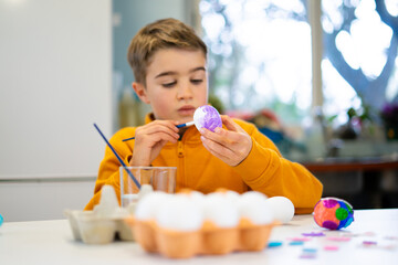 Child painting easter eggs at home with purple paint and brush