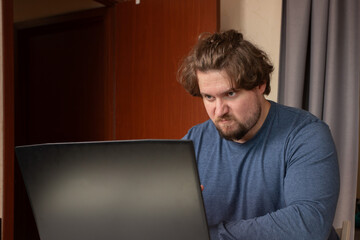 Angry man working on laptop, stress from remote work, emotion-driven reaction at desk