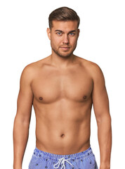 Fototapeta premium Shirtless young man in swimsuit against a studio backdrop, embodying summer vibes