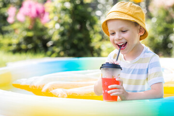 It's a hot summer day. Cute boy swims in the pool. The child drinks refreshing lemonade. The...
