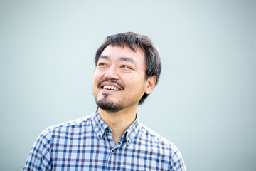 Fototapeta premium Smiling Taiwanese man with beard, looking away in a checkered shirt against a plain background