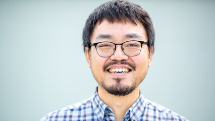 Obraz premium Portrait of a smiling Asian man with glasses in a checkered shirt against a plain background