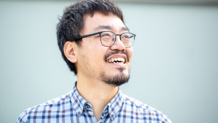 Asian man smiling with glasses in a checkered shirt looking away against a plain background