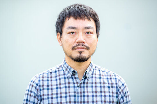 Portrait of a serious Asiatic man with beard in a checkered shirt against a plain background