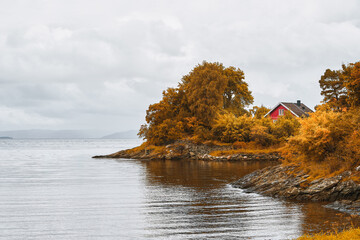 Charming red wooden remote house among colorful trees by a Swedish or Norwegian lake, evoking peace...