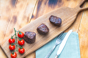 Grilled filet mignon steaks on a wooden board with cherry tomatoes on the table with napkin and...