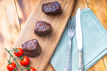 Grilled filet mignon steaks on a wooden board with cherry tomatoes on the table with napkin and...