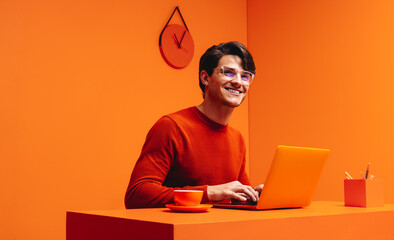 Smiling man working on laptop in a vibrant monochromatic orange office setting