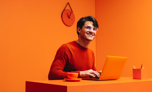 Smiling man working on laptop in a vibrant monochromatic orange office setting