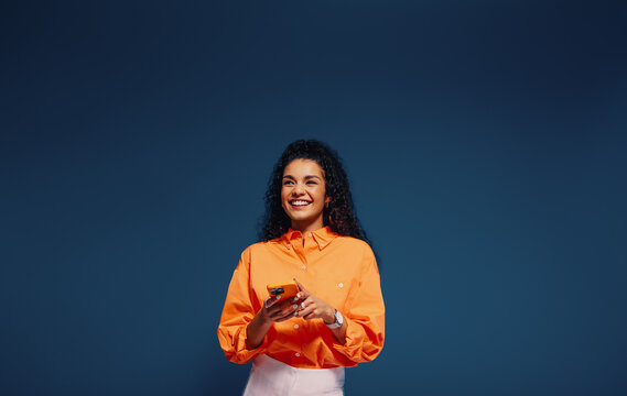 Happy young woman texting in vibrant orange and blue colorblocking outfit